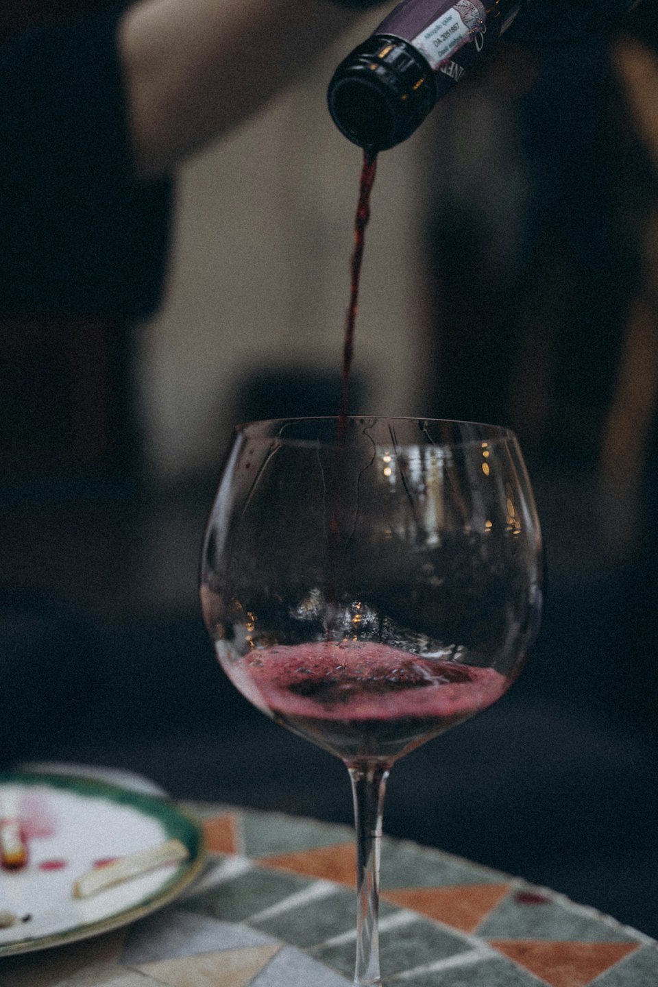 Red wine being poured into a clear glass at a table.